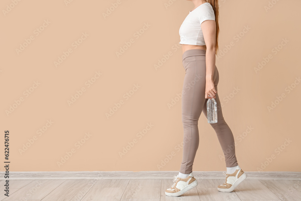 Young woman in sportswear and with bottle of water near beige wall