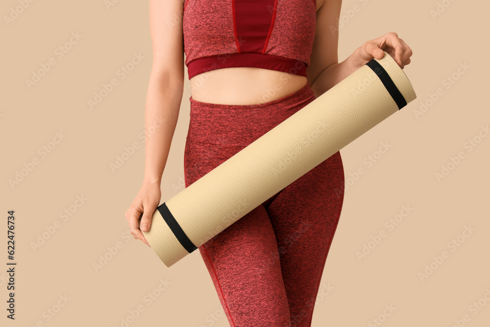 Young woman in sportswear and with yoga mat on beige background