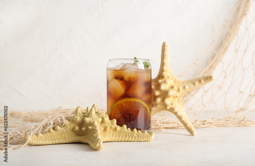 Glass of cold Cuba Libre cocktail and starfishes on white background