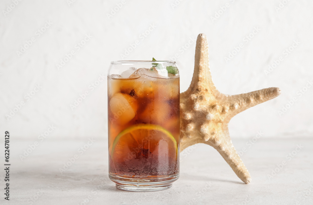 Glass of cold Cuba Libre cocktail and starfish on white background