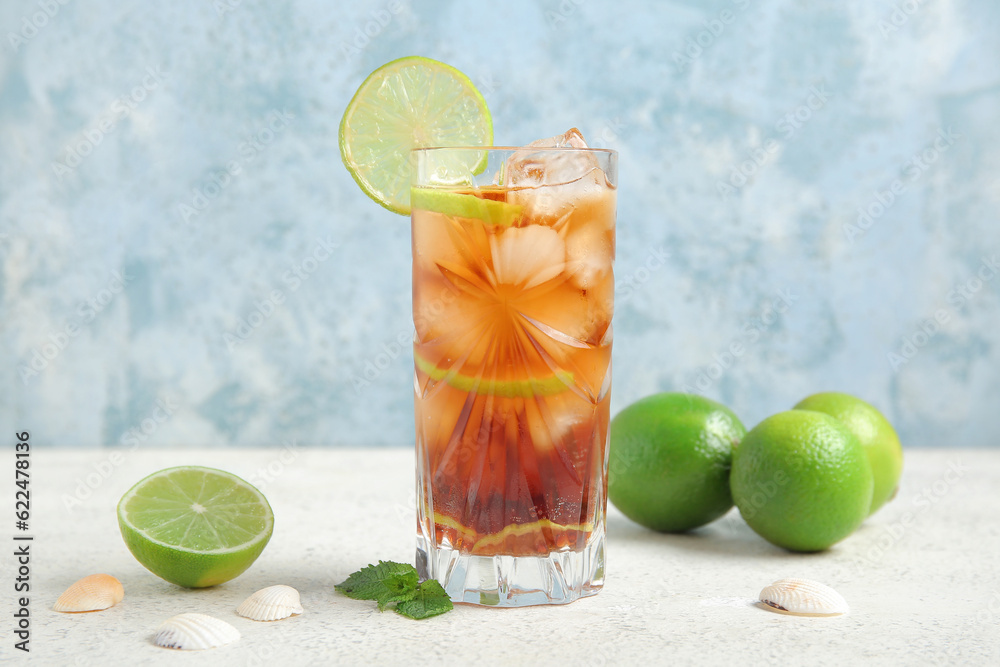 Glass of cold Cuba Libre cocktail and seashells on white table