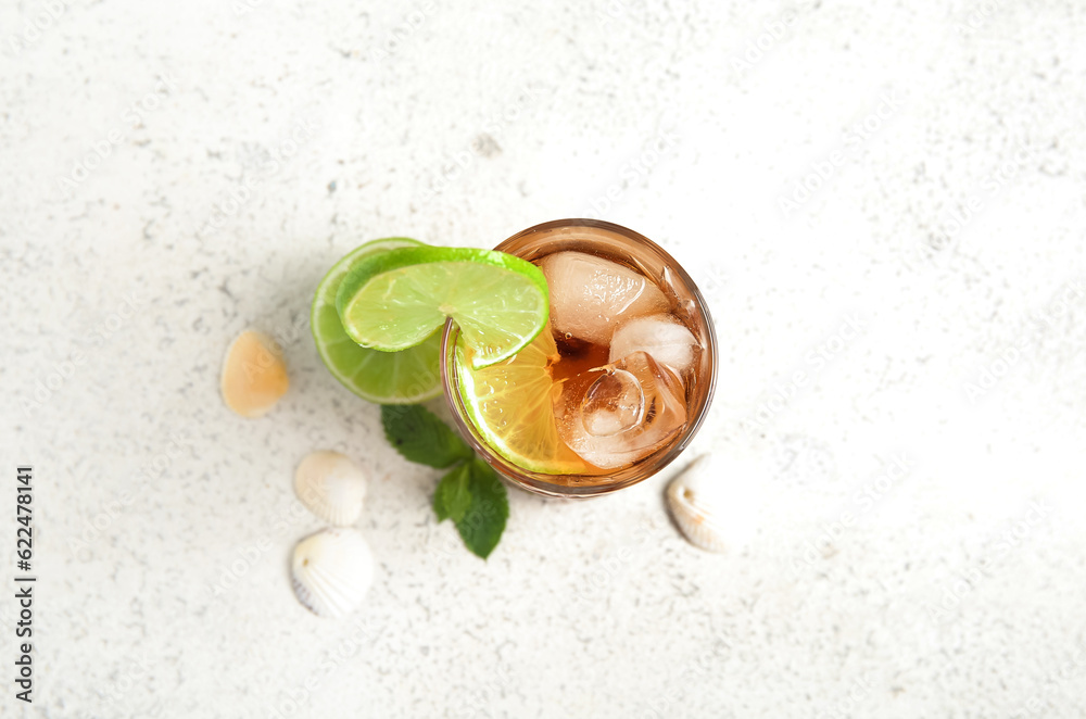 Glass of cold Cuba Libre cocktail and seashells on white background