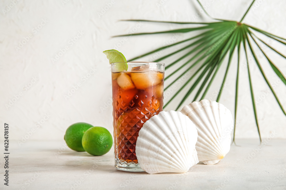 Glass of cold Cuba Libre cocktail, seashells and palm leaf on white background