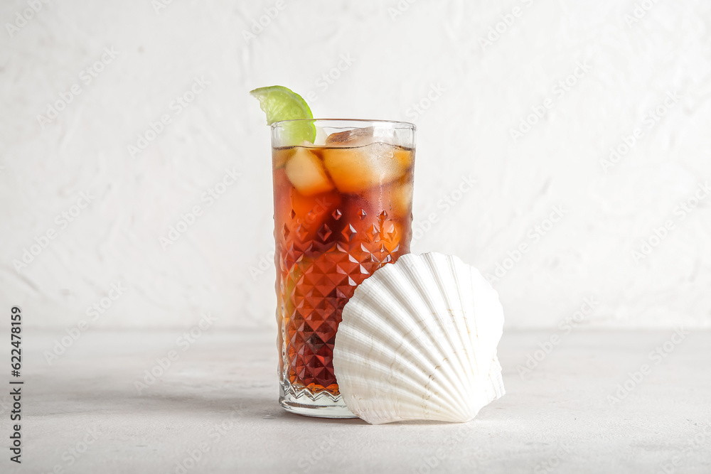 Glass of cold Cuba Libre cocktail and seashell on white background