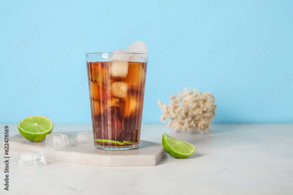 Board with glass of cold Cuba Libre cocktail and coral on white table