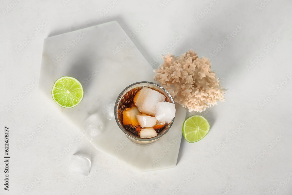 Board with glass of cold Cuba Libre cocktail and coral on white background