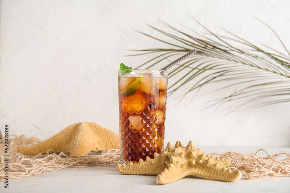 Glass of cold Cuba Libre cocktail, starfishes and palm leaf on white background