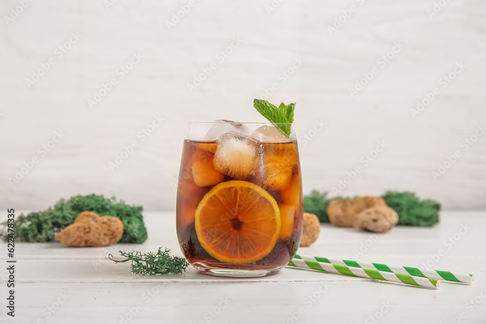 Glass of cold Cuba Libre cocktail, green moss and stones on white wooden table