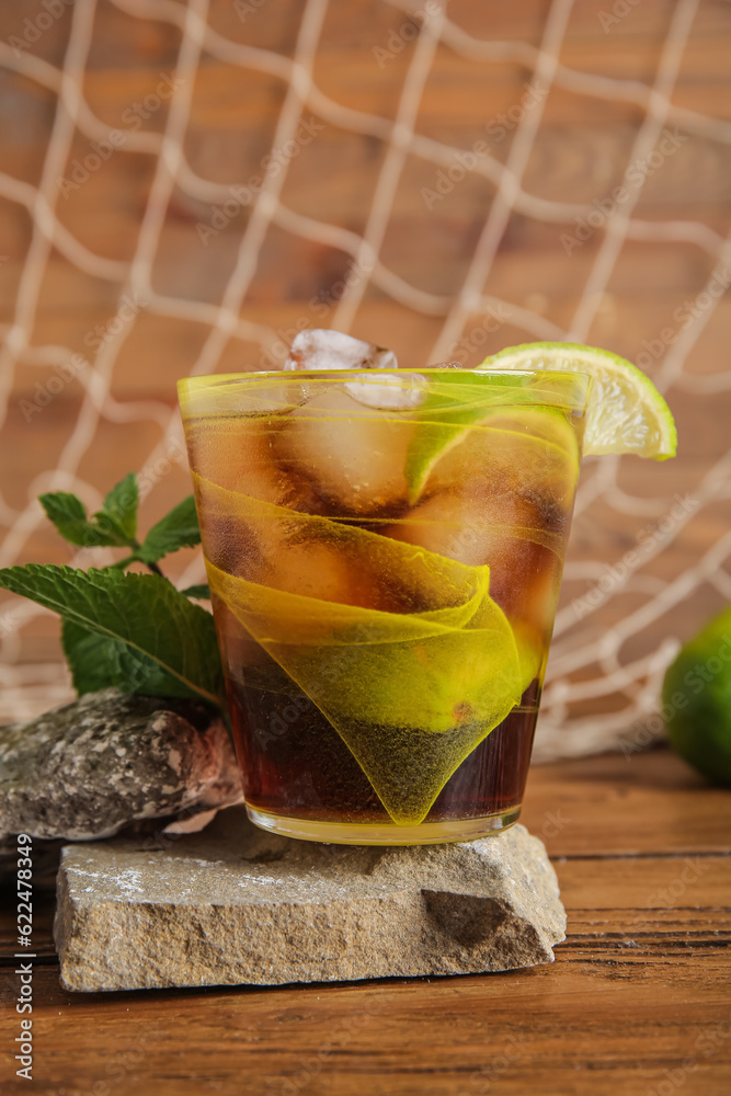 Stones with glass of cold Cuba Libre cocktail and net on wooden background