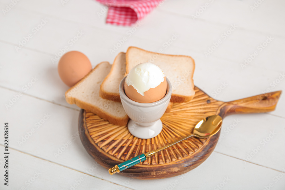 Holder with boiled chicken egg and bread on white wooden background