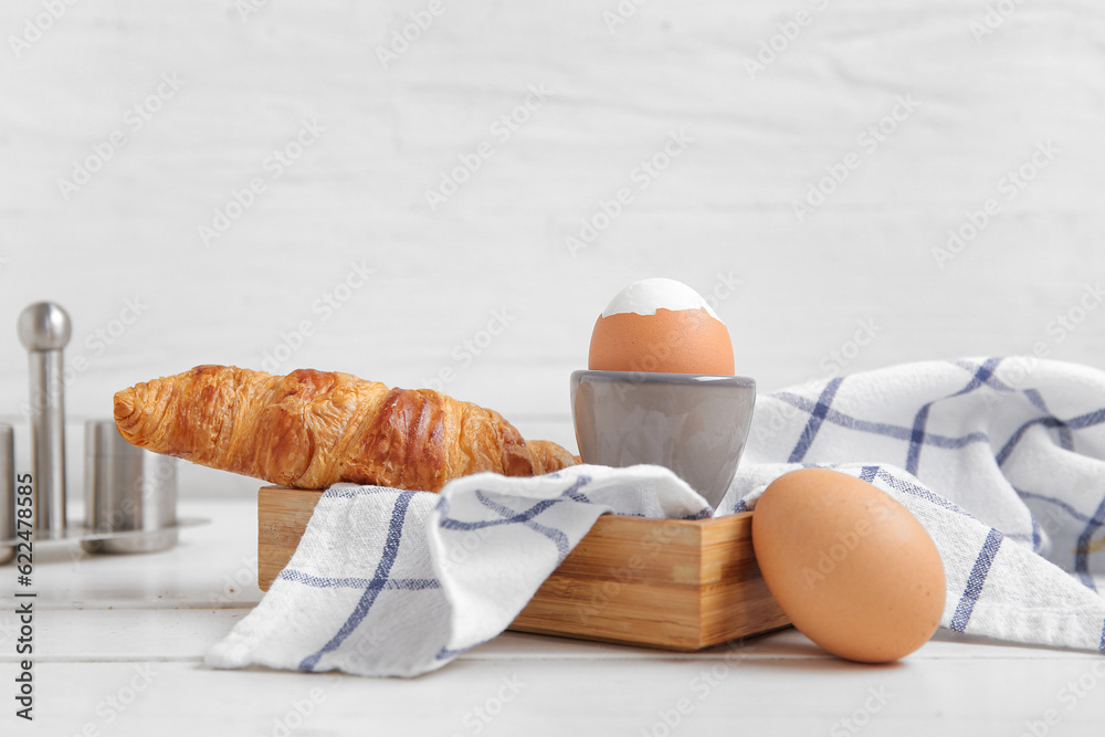 Holder with boiled chicken egg and croissant on white wooden background