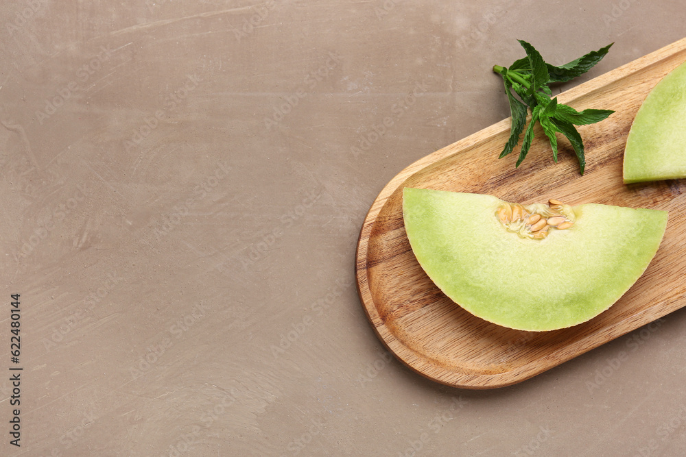 Wooden board with pieces of sweet melon and mint on brown background