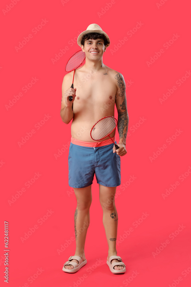 Young man with rackets on red background