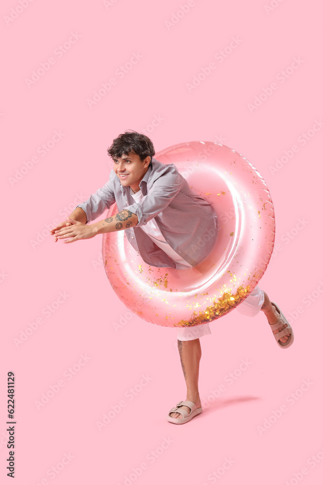 Young man with swim ring on pink background