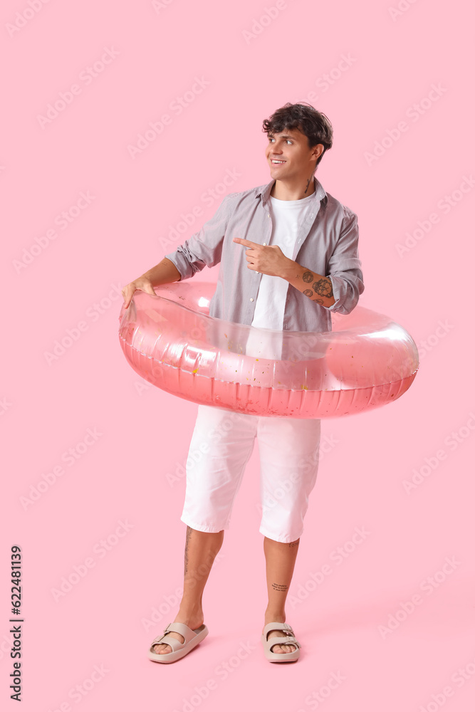 Young man with swim ring pointing at something on pink background