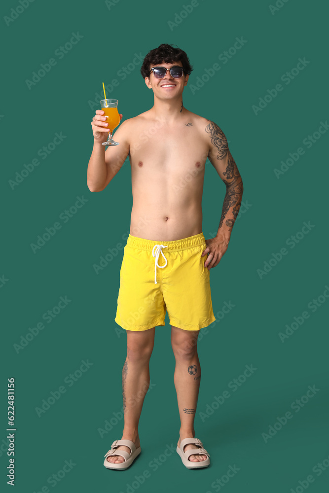 Young man with summer cocktail on green background