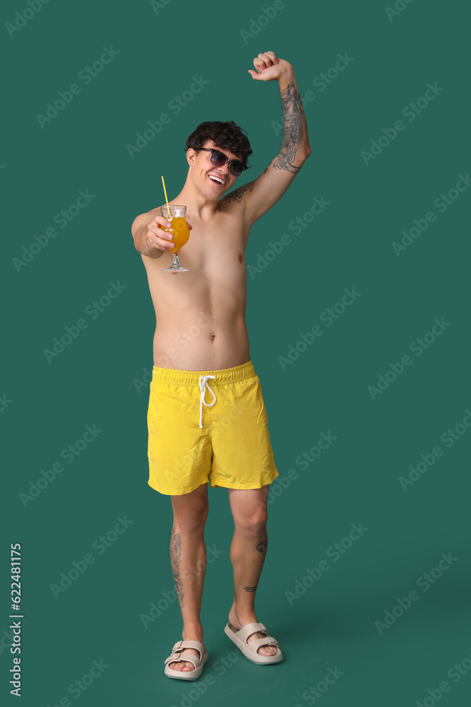 Young man with summer cocktail on green background