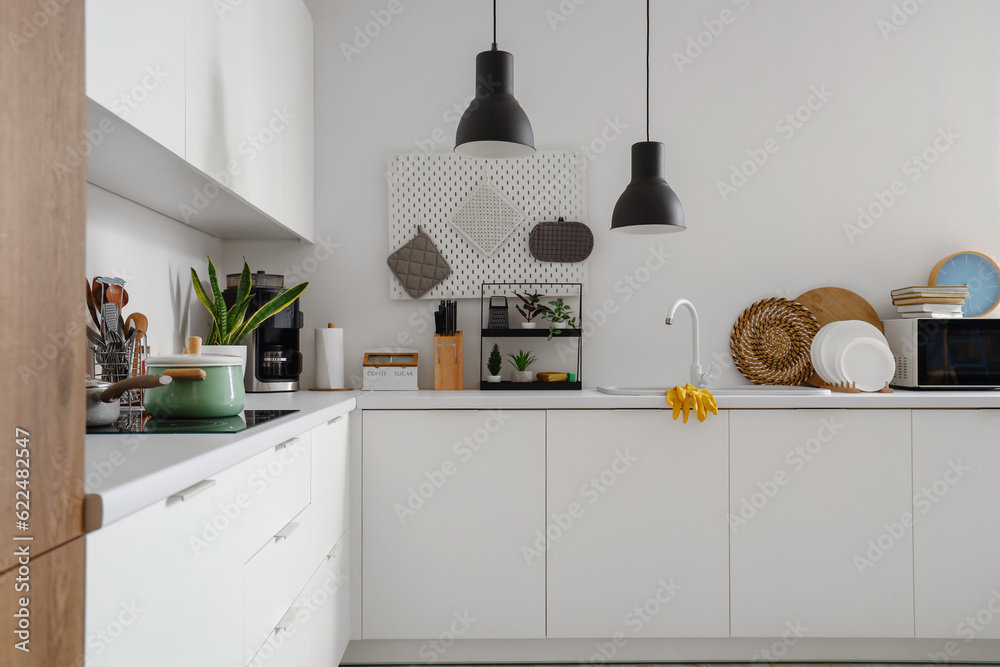 Interior of modern kitchen with white counters, sink, plate rack and utensils