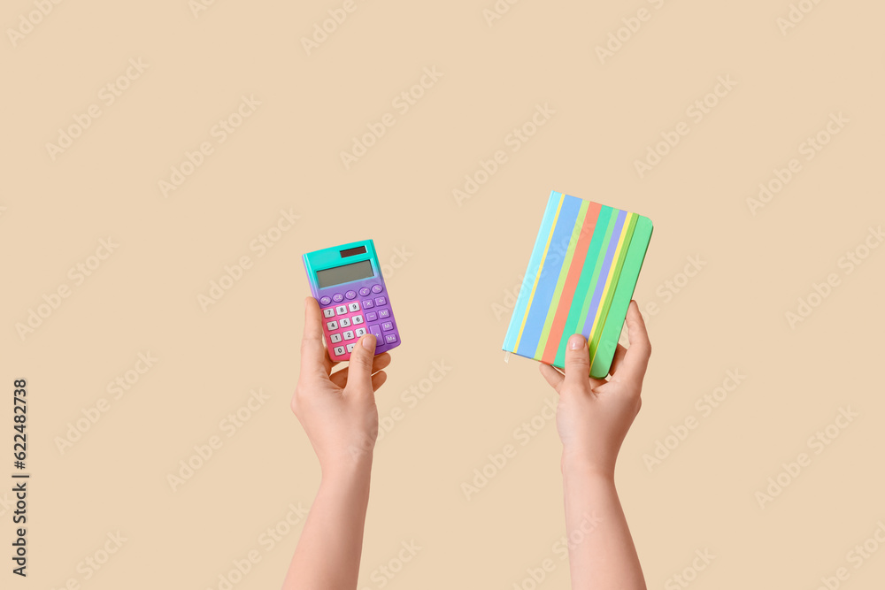 Female hands holding calculator and notebook on beige background