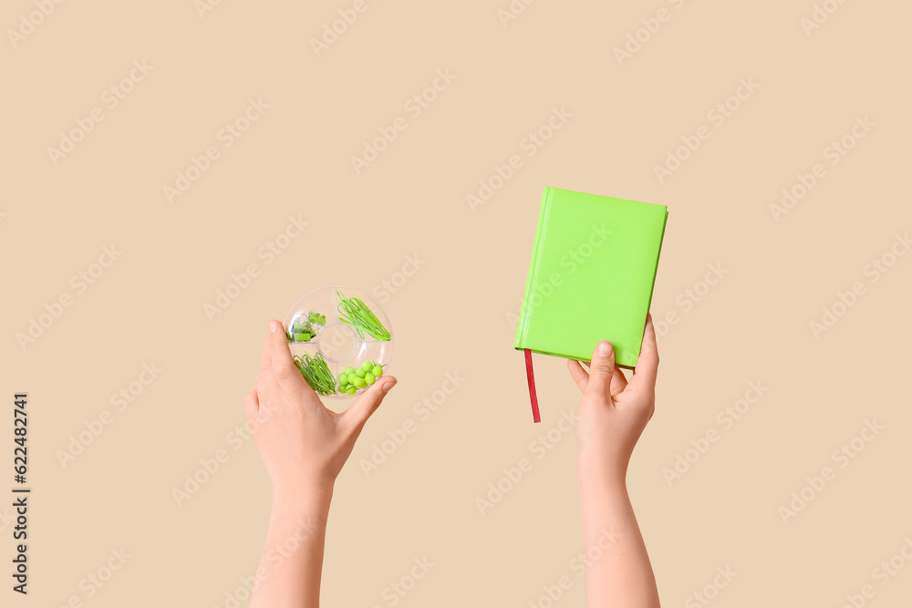 Female hands holding book and case with stationery on beige background