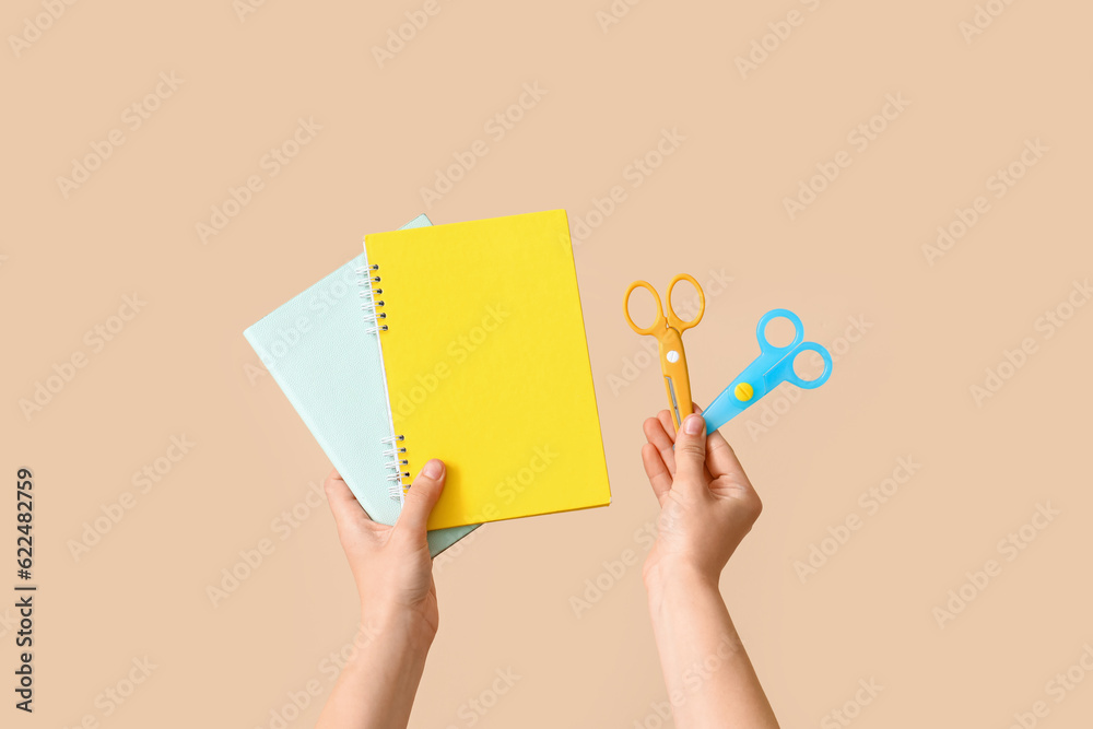 Female hands holding scissors and copybooks on beige background