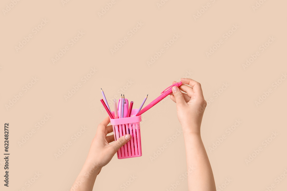 Female hands holding cup with pencils on beige background