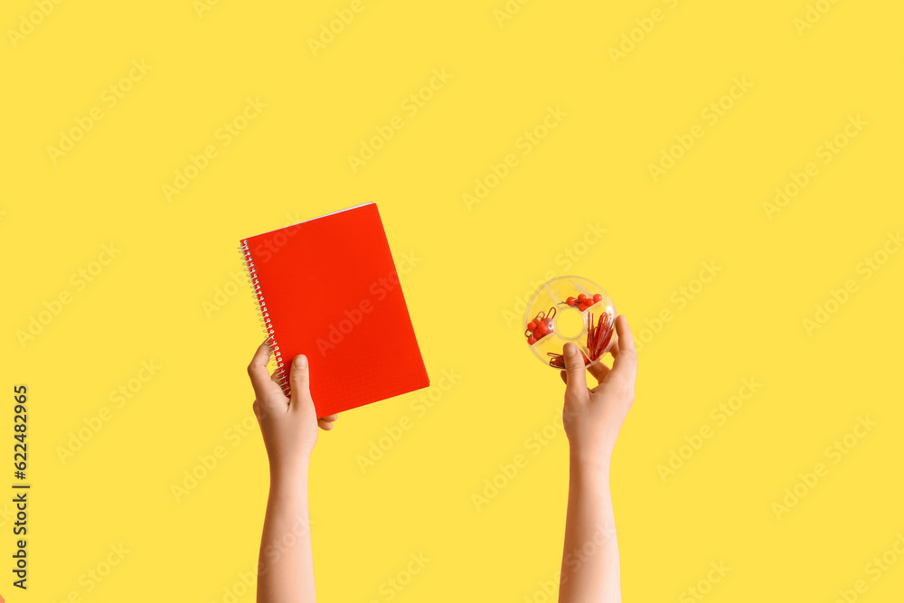 Female hands holding notebook and case with stationery on yellow background