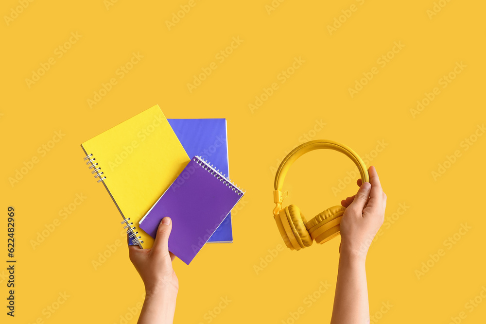 Female hands holding copybooks and headphones on yellow background