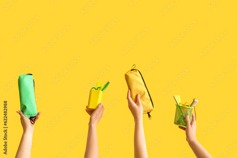 Female hands holding school supplies on yellow background