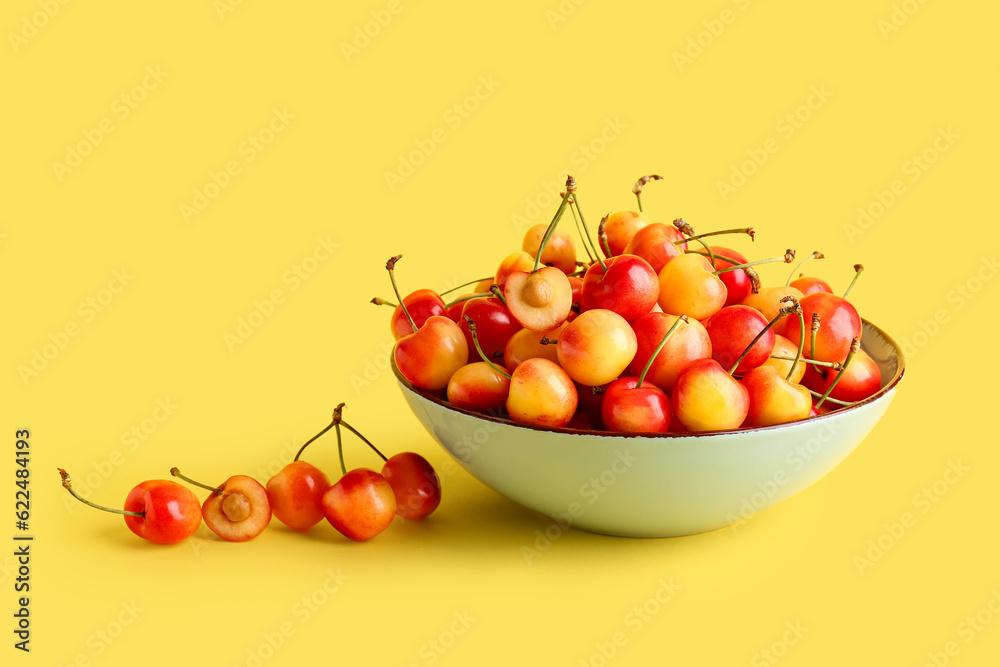 Bowl with sweet yellow cherries on color background