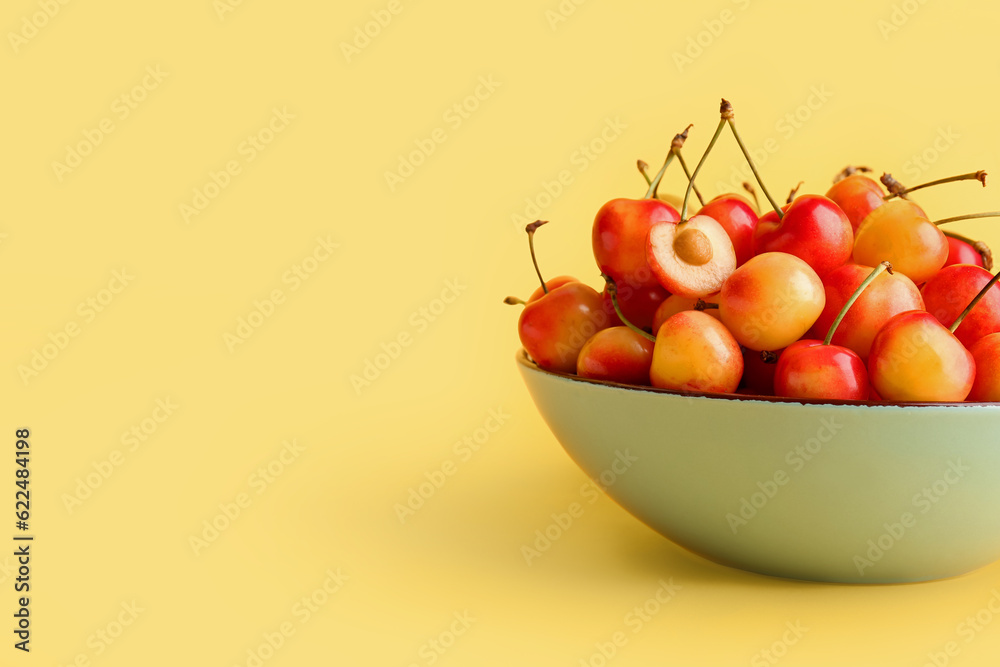 Bowl with sweet yellow cherries on color background