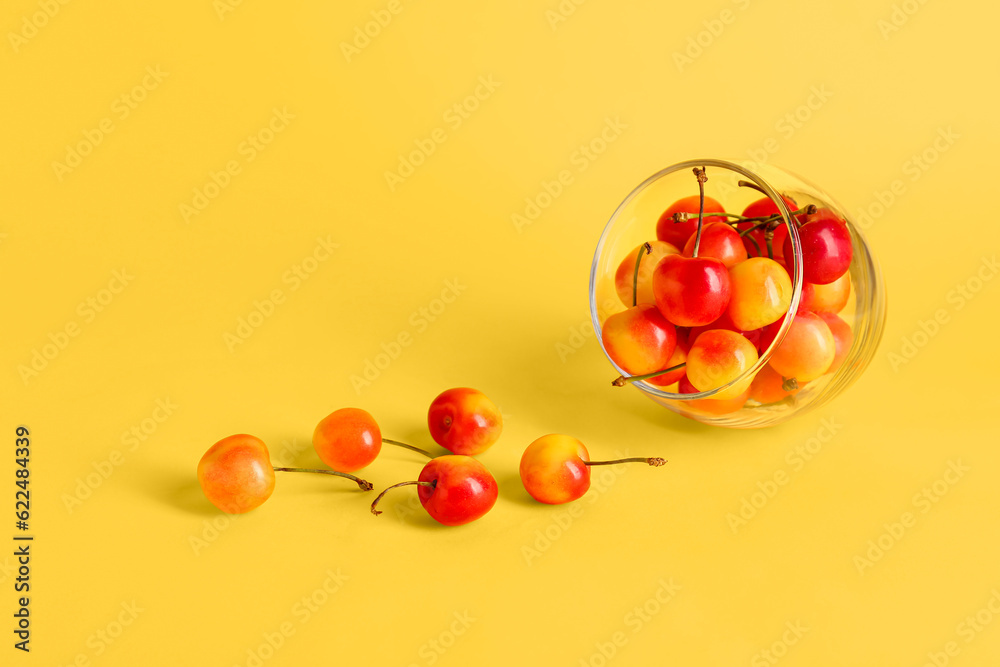 Glass with sweet yellow cherries on color background