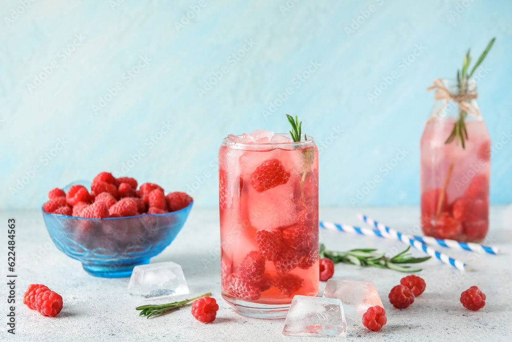 Glass and bottle of fresh raspberry lemonade with rosemary on white table