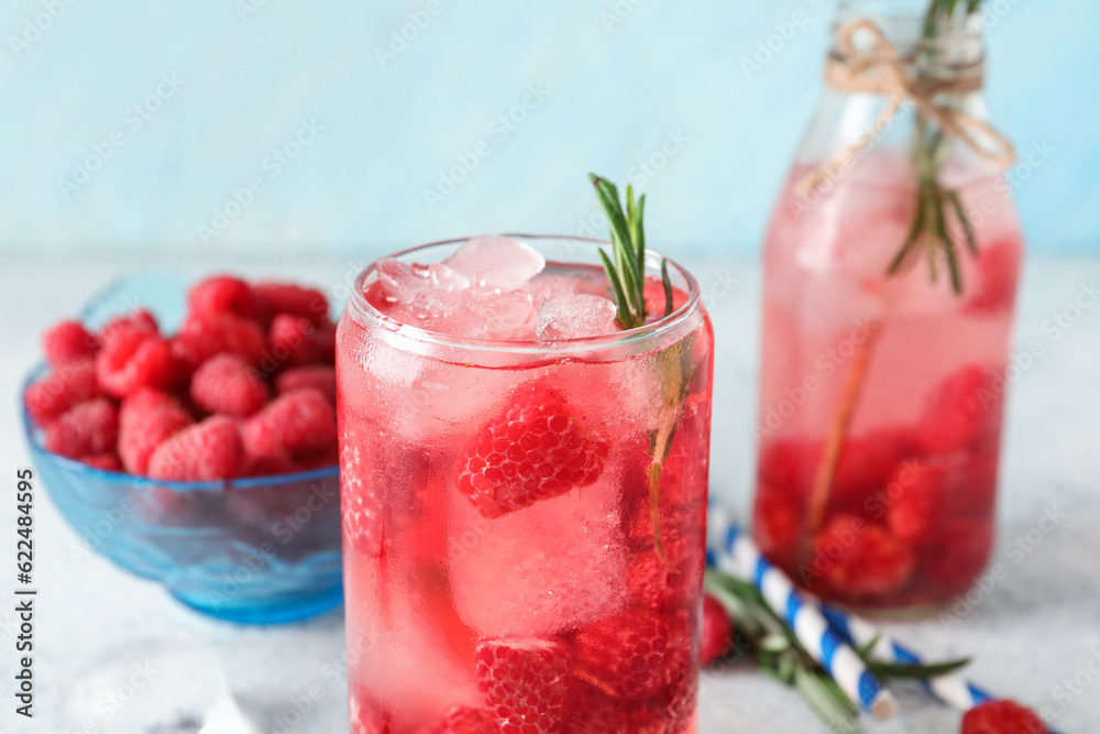 Glass and bottle of fresh raspberry lemonade with rosemary on white table