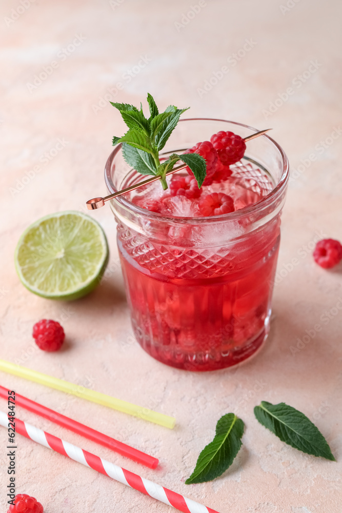 Glass of fresh raspberry lemonade with mint and lime on pink background