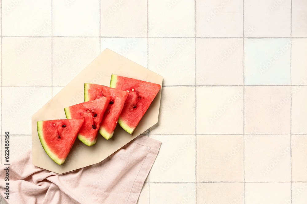 Board with pieces of fresh watermelon on white tile background