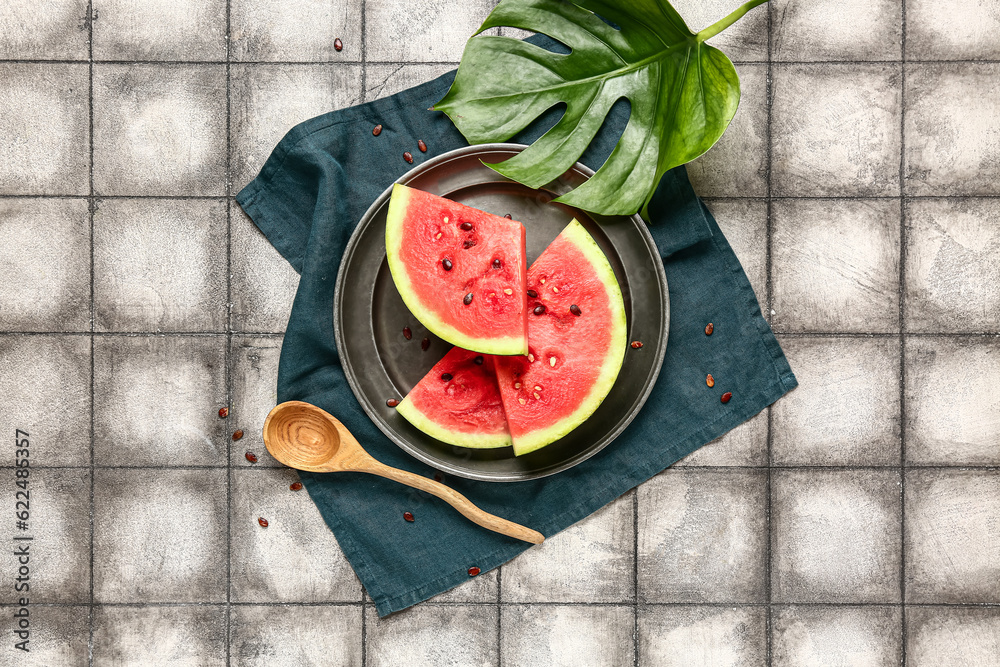 Plate with pieces of fresh watermelon and seeds on grey tile background