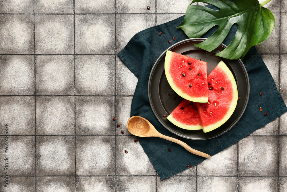 Plate with pieces of fresh watermelon and seeds on grey tile background