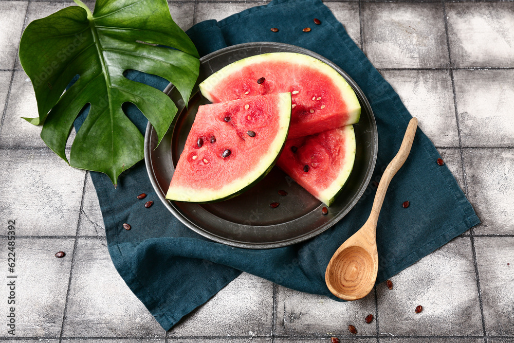 Plate with pieces of fresh watermelon and seeds on grey tile background