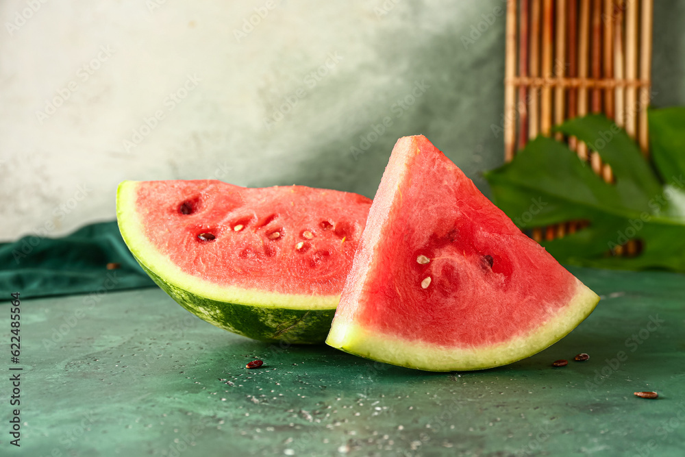 Pieces of fresh watermelon and palm leaf on green table