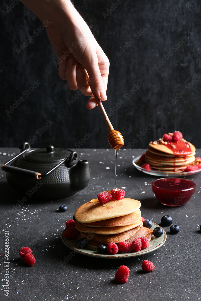 Woman adding honey onto tasty pancakes with raspberries and blueberries on black background