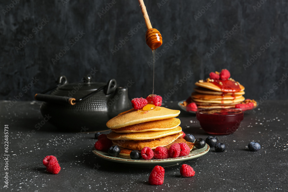 Adding honey onto tasty pancakes with raspberries and blueberries on black background