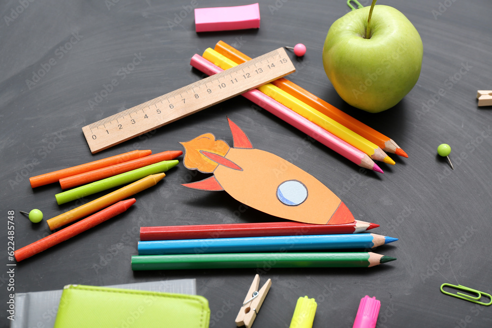 Paper rocket with school stationery and apple on black background