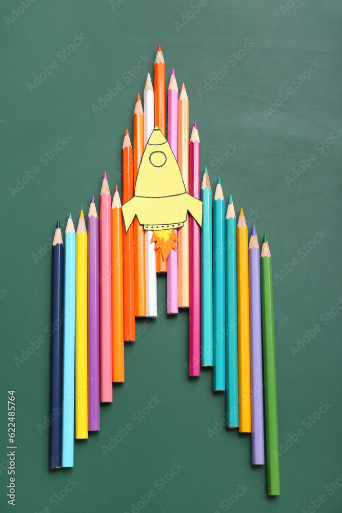 Pencils with paper rocket on green background