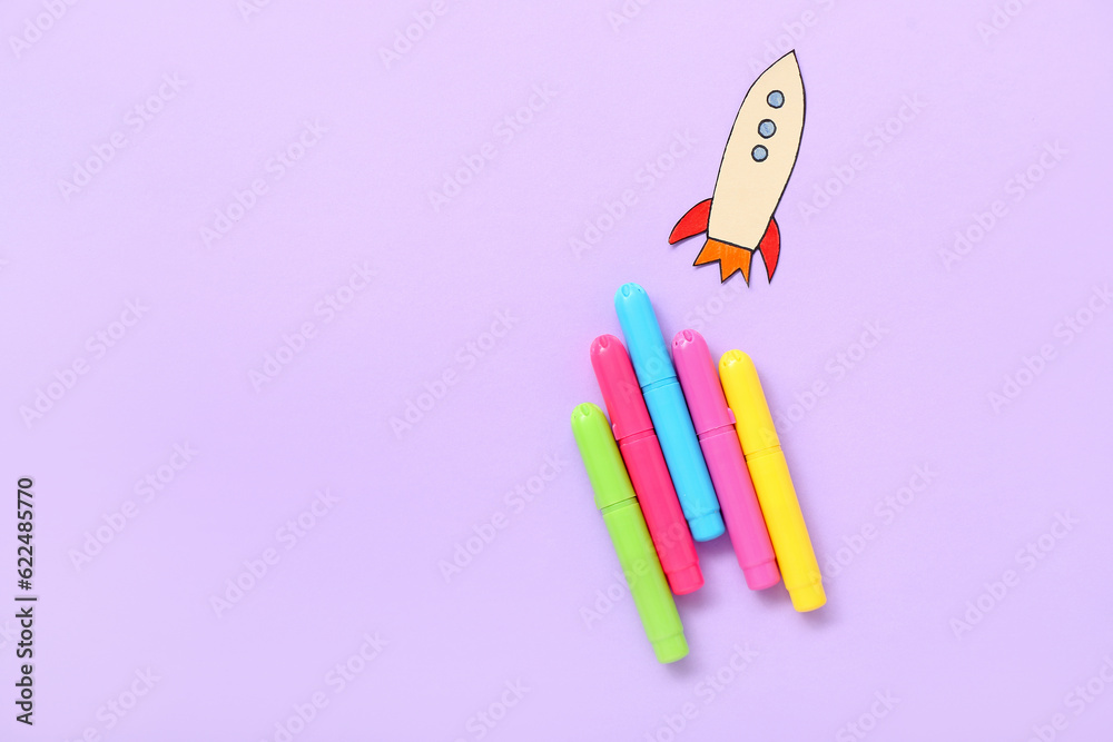 Markers with paper rocket on purple background