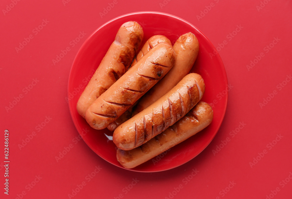 Plate with tasty grilled sausages on red background