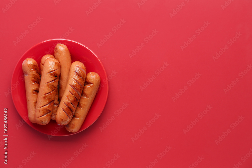 Plate with tasty grilled sausages on red background