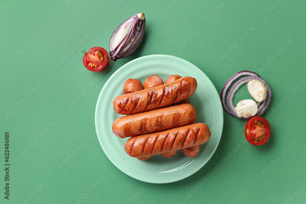 Plate with tasty grilled sausages on green background