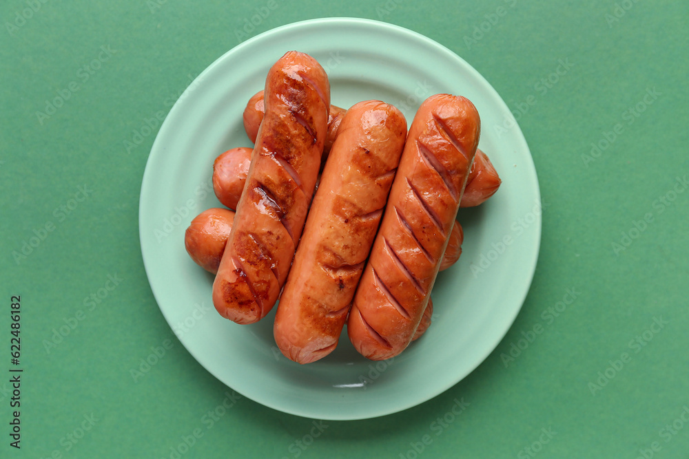 Plate with tasty grilled sausages on green background