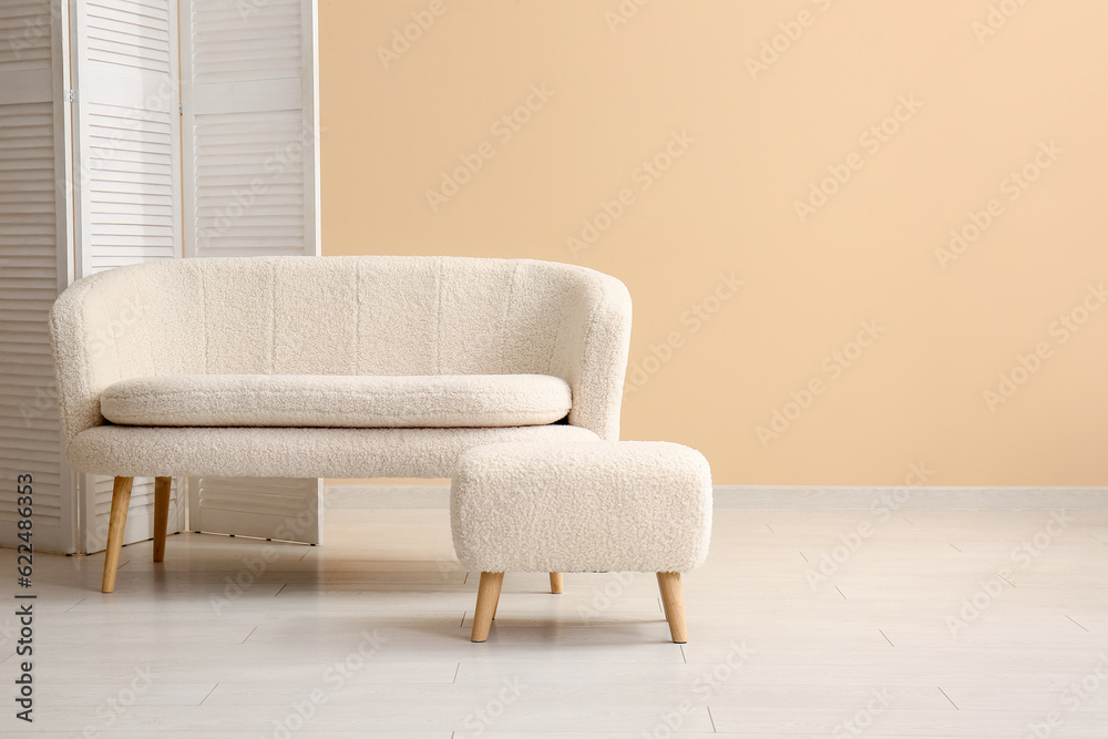 Cozy white sofa with ottoman and folding screen near beige wall